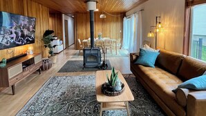 A cozy living room with a wooden ceiling, a large TV, a sofa, a coffee table, and a fireplace.