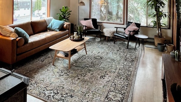 A cozy living room with a wooden ceiling, a brown leather sofa, a coffee table, and a patterned rug.