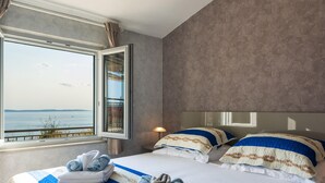 A hotel room with a large bed, a view of the sea, and a window with curtains.