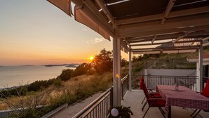 A terrace with a table and chairs, overlooking a coastal view during sunset.