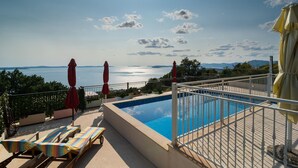 A poolside area with a view of the sea, lounge chairs, and umbrellas.