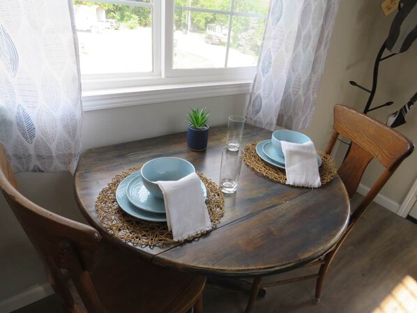 A round wooden dining table with two blue plates, a glass, and a small potted plant.