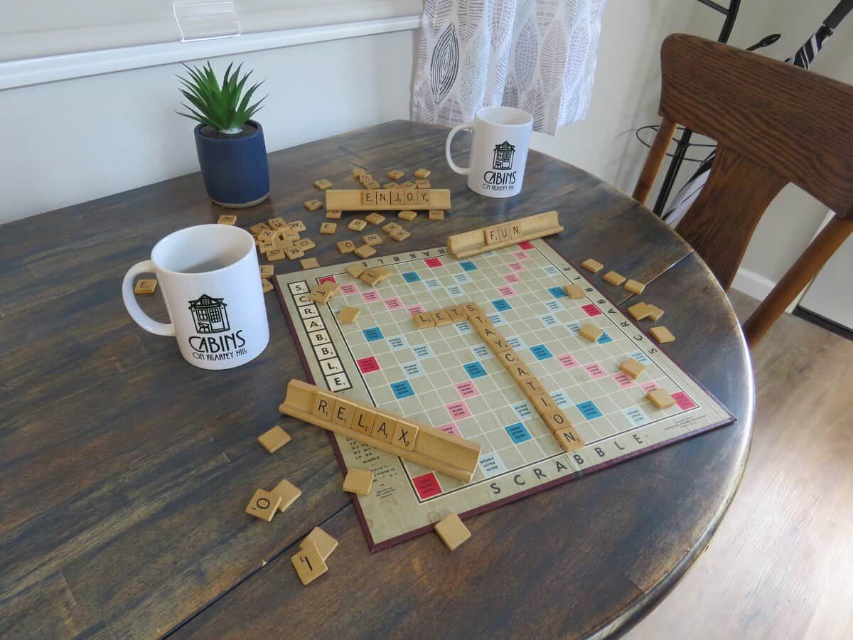 Un juego de Scrabble sobre una mesa redonda de madera, con una taza de café y una planta en maceta.