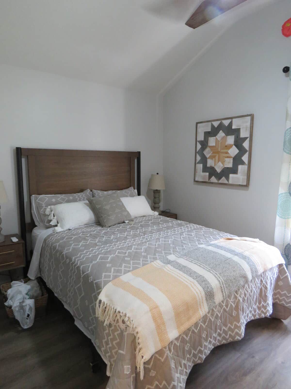 A bedroom with a wooden headboard, a bed with patterned bedding, a bedside lamp, and a wall-mounted decorative piece.