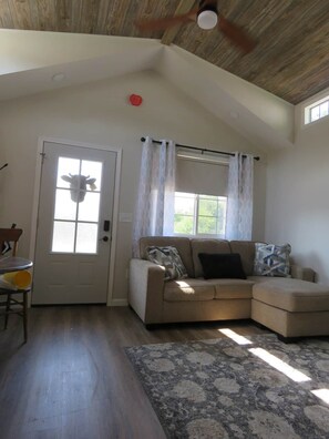 A living room with a beige sectional sofa, a patterned rug, a wooden ceiling, and a door with a window.