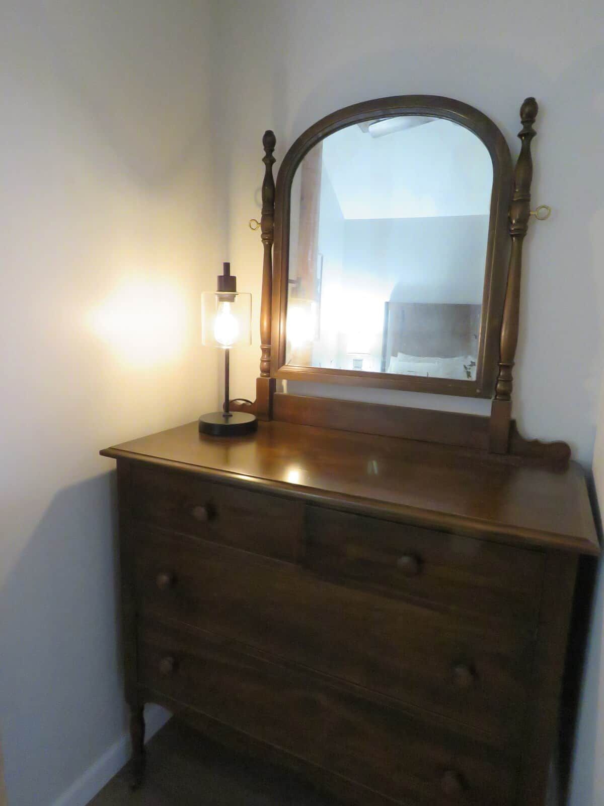 A wooden dresser with a mirror and a light fixture.