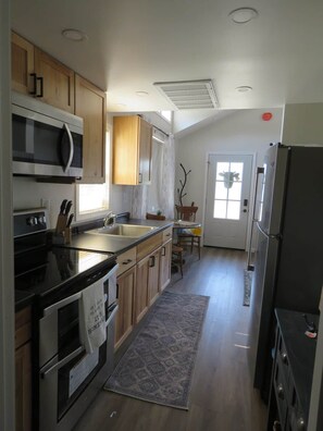 Una cocina con armarios de madera, microondas, refrigerador y pileta.