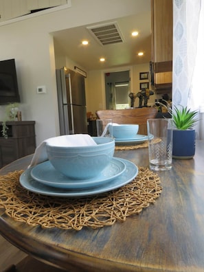 Una mesa de comedor con platos y tazones azules, un mantel tejido y una planta en maceta.