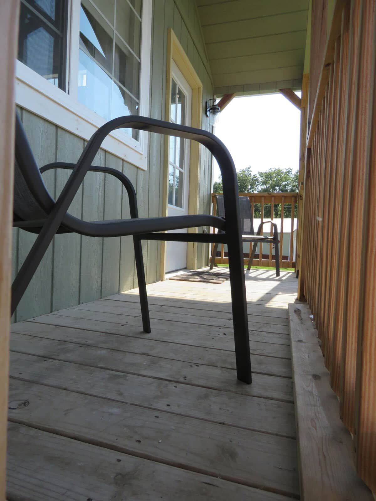 A wooden deck with a metal chair and a table, leading to a building with large windows.