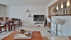 Una sala moderna con una mesa de comedor de madera, un televisor y un sofá blanco.