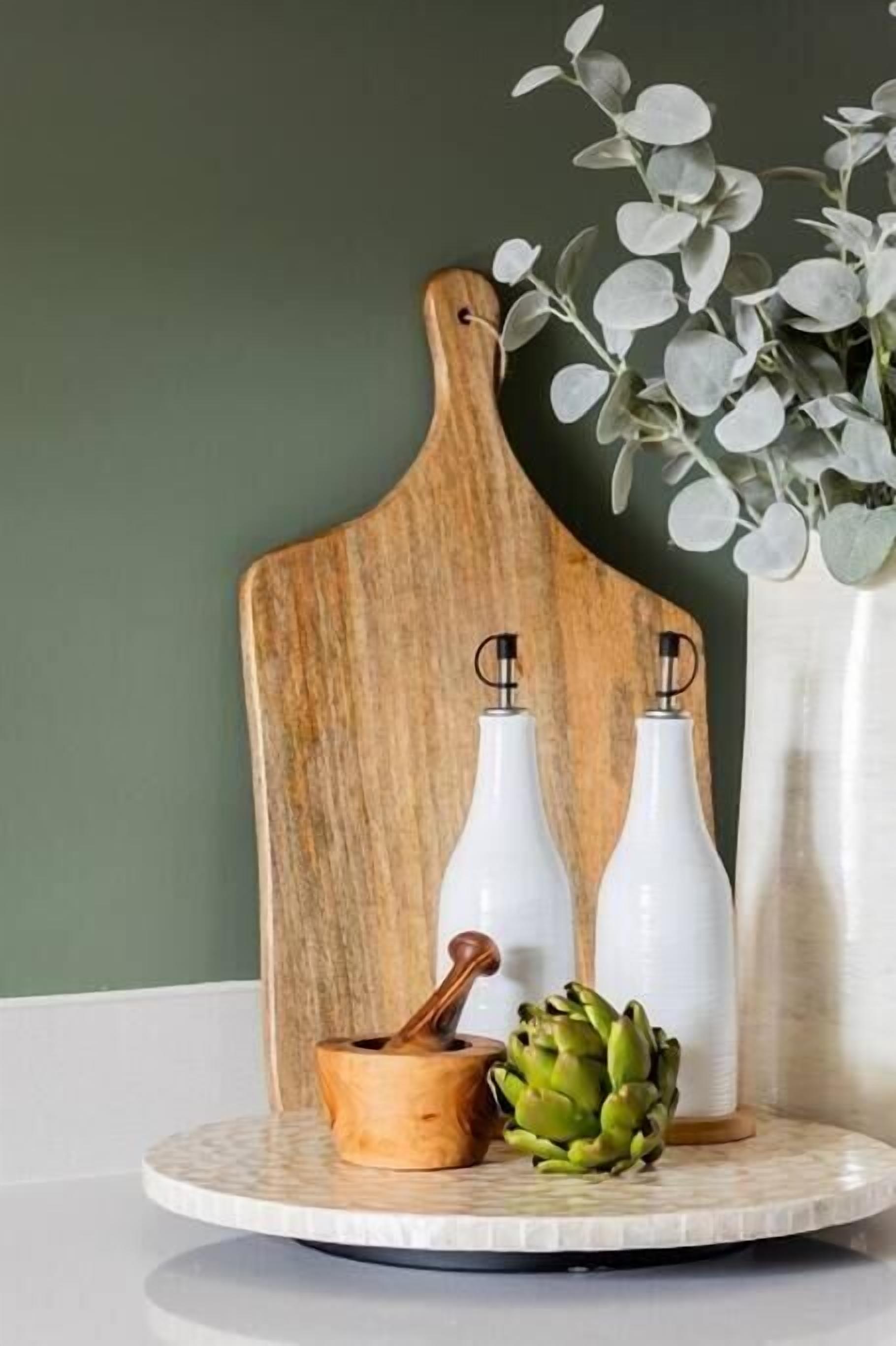 A wooden cutting board with two white bottles and a wooden spoon on a round table.
