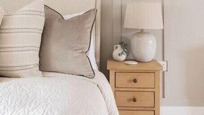 Ein Schlafzimmer mit einem Bett, Kissen, einem Nachttisch mit Lampe und einem an der Wand hängenden abstrakten Gemälde.