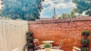 Eine Holzterrasse mit einem runden Tisch und sechs Stühlen, umgeben von einer Ziegelmauer und Blumentöpfen.