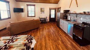 A spacious living area with a wooden ceiling, a sofa, a dining table, and a kitchen with a stove and refrigerator.