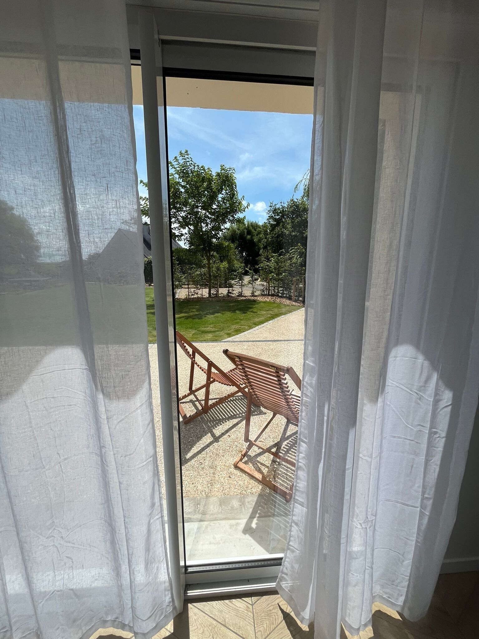 Une porte-fenêtre coulissante donne sur un espace extérieur aménagé en terrasse, avec un banc en bois et une pelouse.