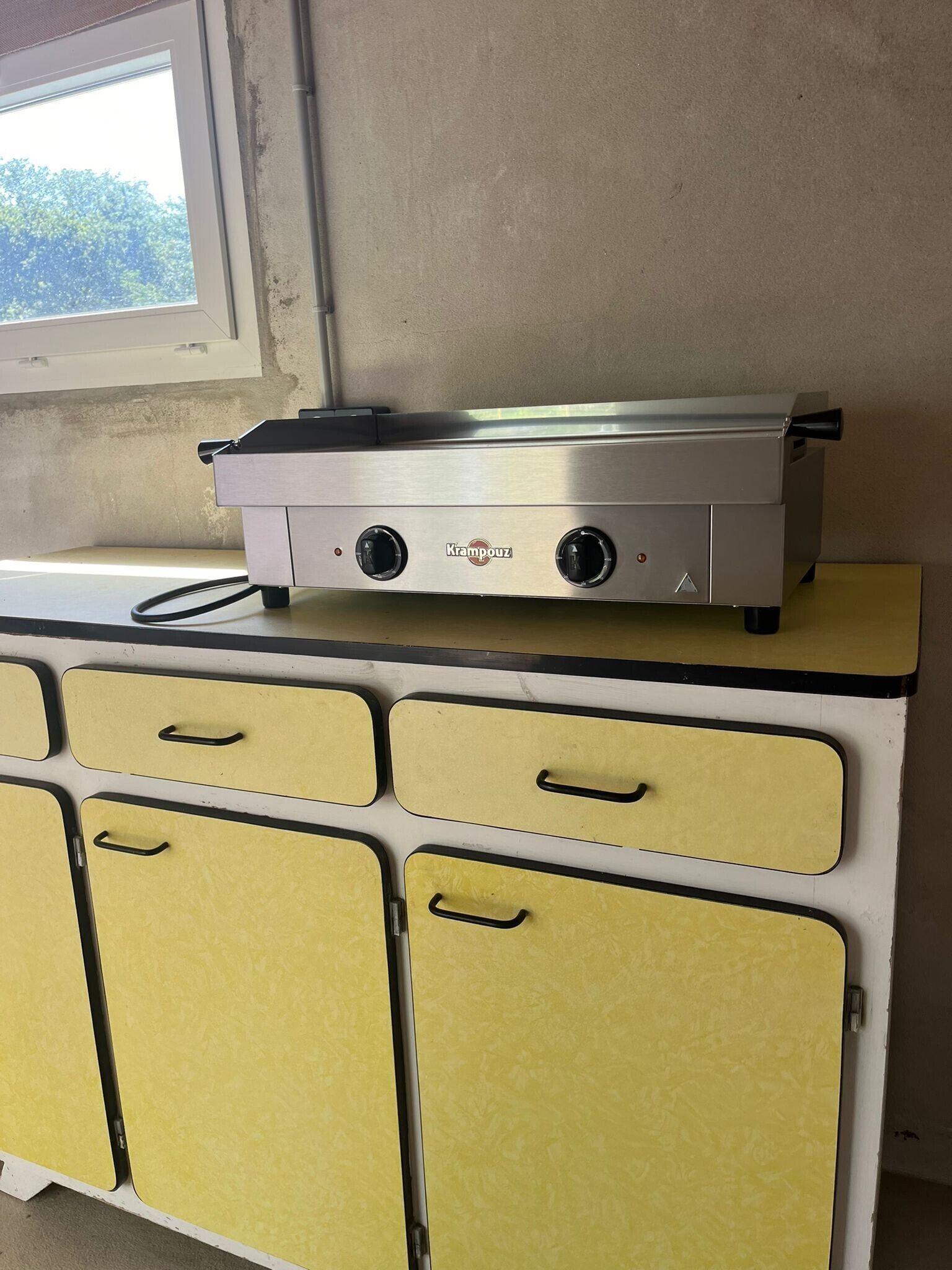 A kitchen with a stainless steel appliance on top of a yellow cabinet with handles.