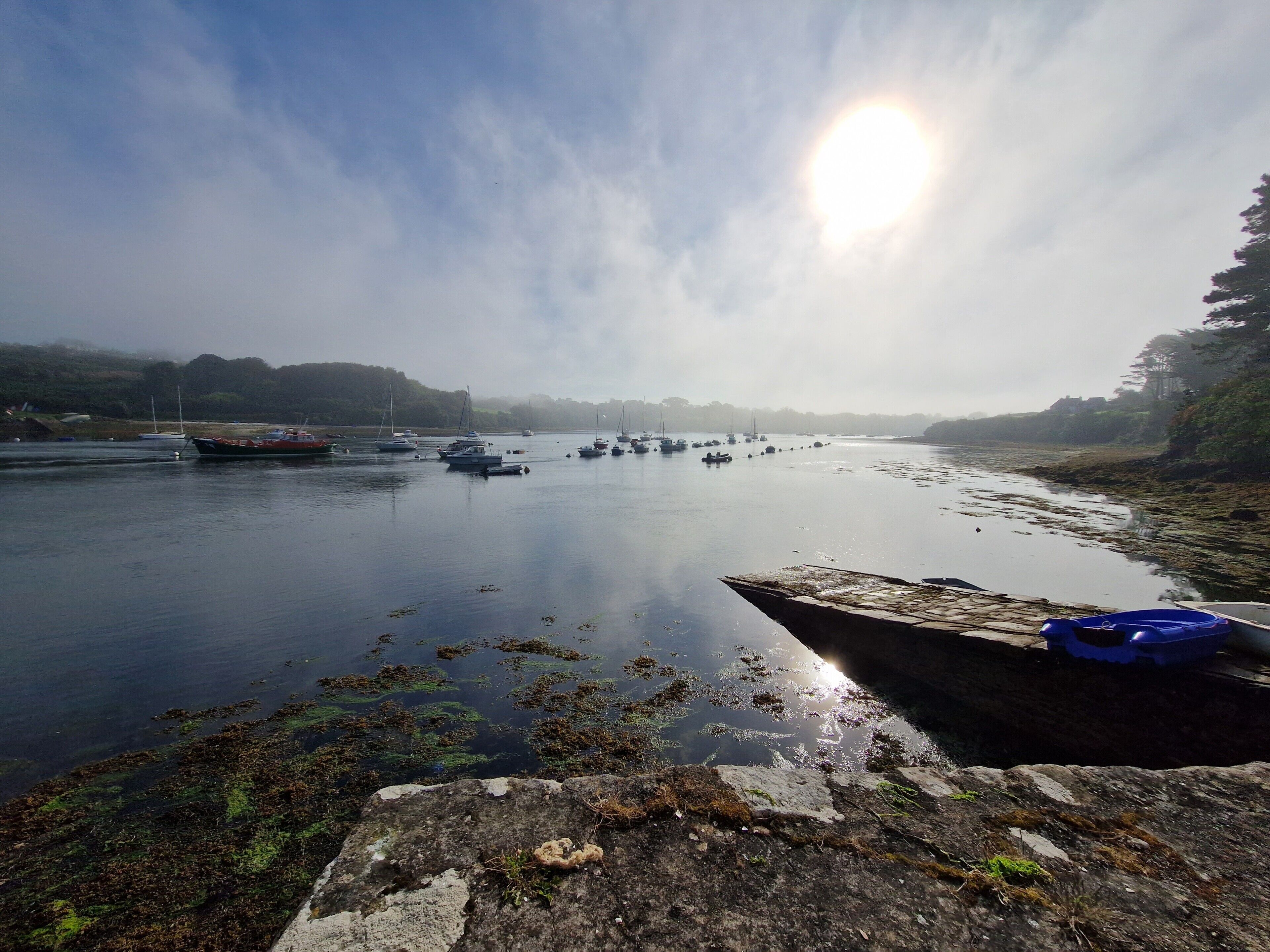 A calm river with boats, a rocky shore, and a clear sky.