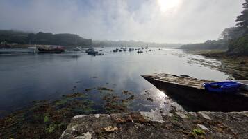 A calm river with boats, a rocky shore, and a clear sky.