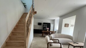 Un vaste espace de vie agrémenté d’un escalier en bois, d’un canapé, d’une table basse et d’une cuisine en arrière-plan.