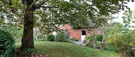 A brick building with a white door, surrounded by a grassy area with trees and shrubs.
