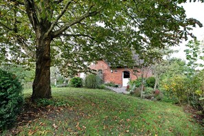 Un bâtiment en briques avec une porte blanche, entouré d’une zone verdoyante avec des arbres et des arbustes.