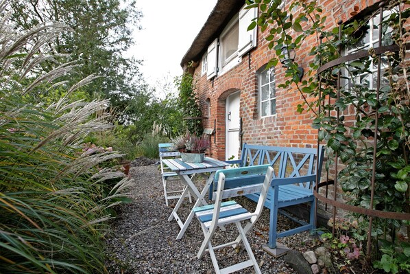 Un espace extérieur aménagé dans un style rustique, avec un bâtiment en briques, un chemin de gravier et de la verdure.