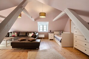 Une chambre à coucher aménagée dans un espace mansardé, avec un plafond en pente, une grande fenêtre, un canapé, un lit, une commode et une lampe.