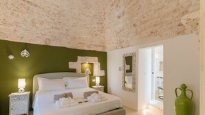 Een slaapkamer met een stenen plafond, een bed met witte lakens, bedlampen en een groene wand.
