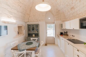 Une cuisine avec des meubles blancs, une table en bois et un plafond en pierre.
