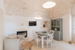 Une pièce avec une cheminée, une table à manger avec des chaises, un téléviseur fixé au mur et un meuble avec des portes en verre.