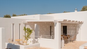 Een wit gebouw met een zwembad, terras en een pergola.