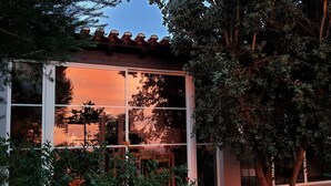 Ein modernes Gebäude mit großen Fenstern, die den Sonnenuntergang reflektieren, umgeben von üppiger Vegetation.