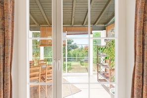 A room with a sliding glass door leading to an outdoor area with a patio table and chairs, a garden view, and a metal plant stand.
