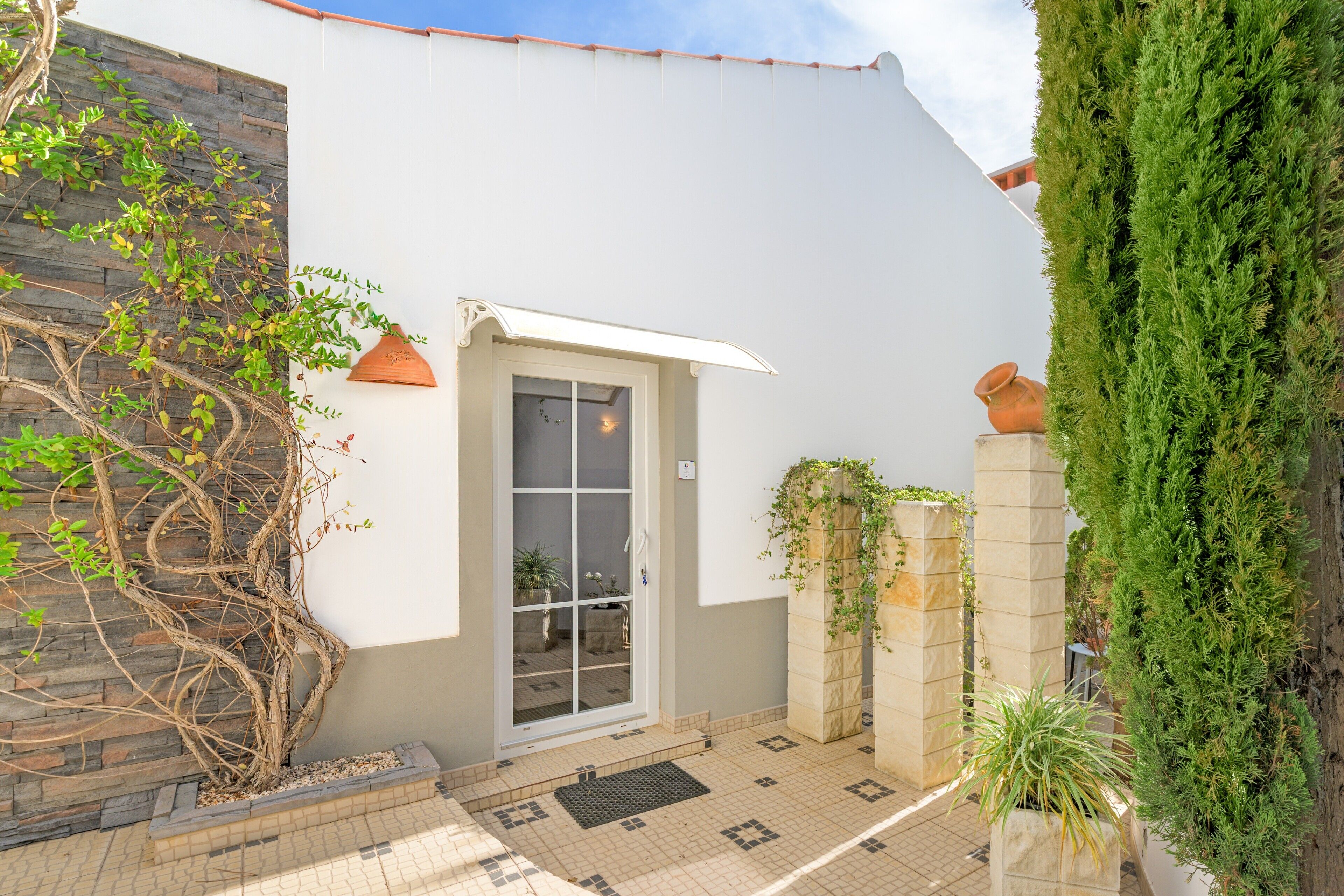 A building with a white exterior, a glass door entrance, tiled flooring, and potted plants.