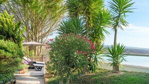 Ein Garten mit einem Pfad zu einer Sitzgruppe, die einen Tisch und Stühle umfasst, umgeben von verschiedenen Pflanzen und Bäumen.