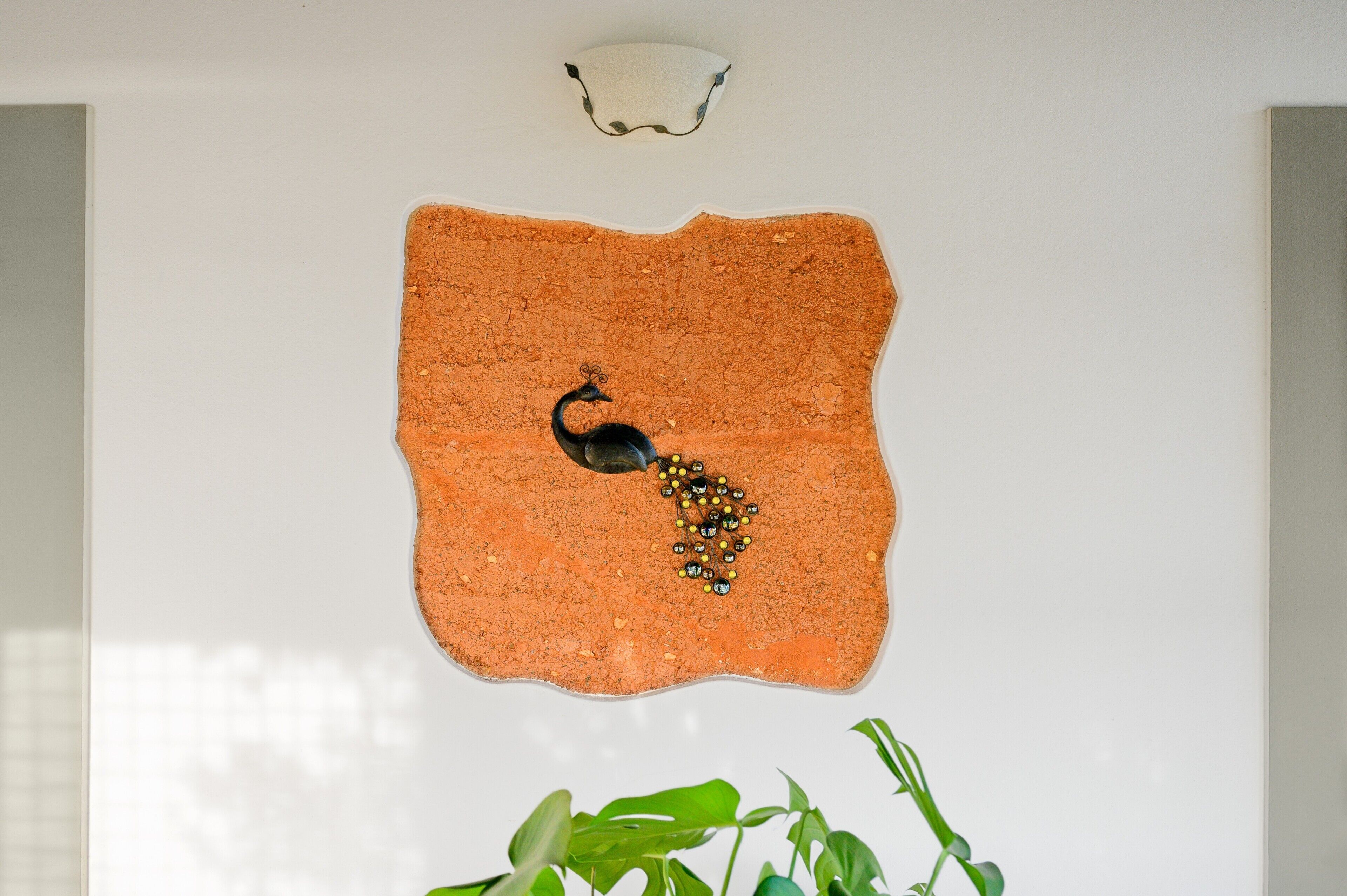 A wall with a textured orange surface, a small black object, and a white light fixture.