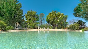 Ein klares Schwimmbecken, umgeben von Bäumen und einem Gebäude mit überdachter Terrasse.