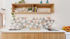Une cuisine avec des meubles de rangement en bois, un plan de travail blanc, un évier, une tablette et un panier de fruits.