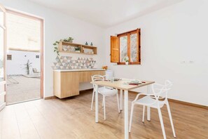 Une cuisine moderne avec un plan de travail en bois, des chaises blanches et une fenêtre dotée de volets en bois.