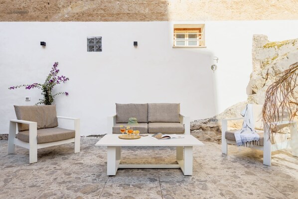 Un mur blanc avec une fenêtre, un canapé blanc, une table basse blanche avec un plateau et des verres, et une chaise avec une plante.