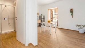 A modern interior with a shower, a dining area with white chairs, and a kitchen in the background. - Apartment 'Travel Rooms-Arenella Piano Terra 1' with Mountain View, Wi-Fi and Air Conditioning (Palermo)
