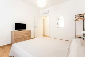 A bedroom with a bed, a TV on a wooden dresser, a wardrobe, a mirror, and a door leading to another room. - Apartment 'Travel Rooms-Arenella Piano Terra 1' with Mountain View, Wi-Fi and Air Conditioning (Palermo)