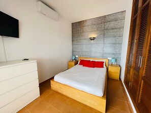 Une chambre à coucher comprenant un lit, des tables de chevet, un téléviseur, une armoire et un luminaire fixé au mur.