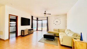 A spacious living room with a sofa, ottoman, TV, and a ceiling fan. - Vacation Home 'Villa Maria' with Mountain View, Wi-Fi and Air Conditioning (Playa Blanca)