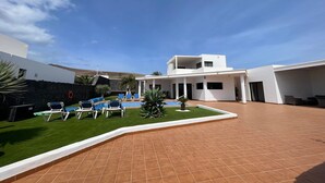 A modern building with a swimming pool, outdoor seating, and a clear sky. - Vacation Home 'Villa Maria' with Mountain View, Wi-Fi and Air Conditioning (Playa Blanca)
