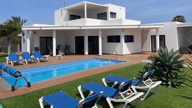 A modern two-story building with a swimming pool, lounge chairs, and a covered patio area. - Vacation Home 'Villa Maria' with Mountain View, Wi-Fi and Air Conditioning (Playa Blanca)