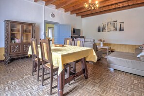 Un comedor con mesa y sillas de madera, un aparador con libros, televisor y sofá.