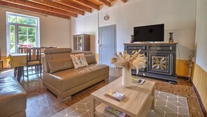 A living room with a sofa, a coffee table with magazines, a TV on a cabinet, and a chandelier. - Le Gîte du Sourcier – Authentic and Welcoming Stay in Dordogne (Sadillac)