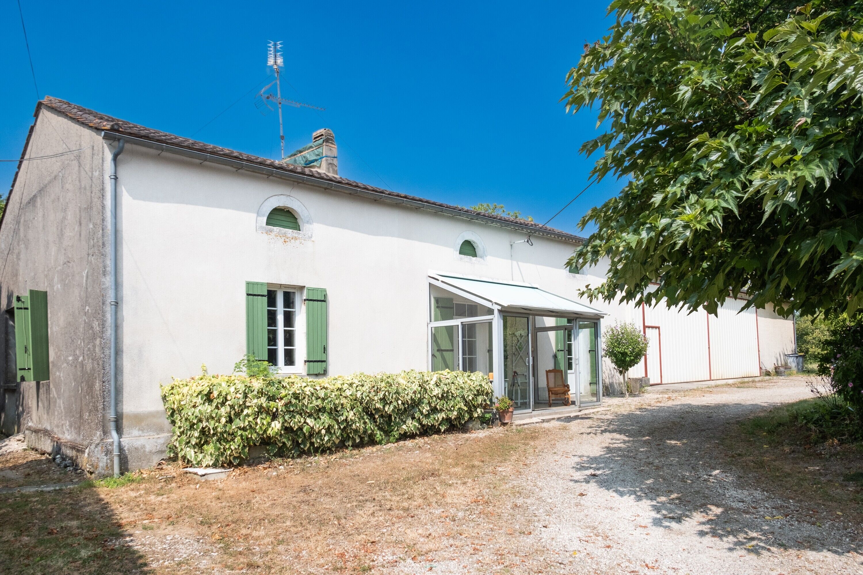 A white building with green shutters, a covered porch, and a gravel driveway.