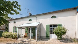 A house with a covered patio, green shutters, and a small tree. - Le Gîte du Sourcier – Authentic and Welcoming Stay in Dordogne (Sadillac)